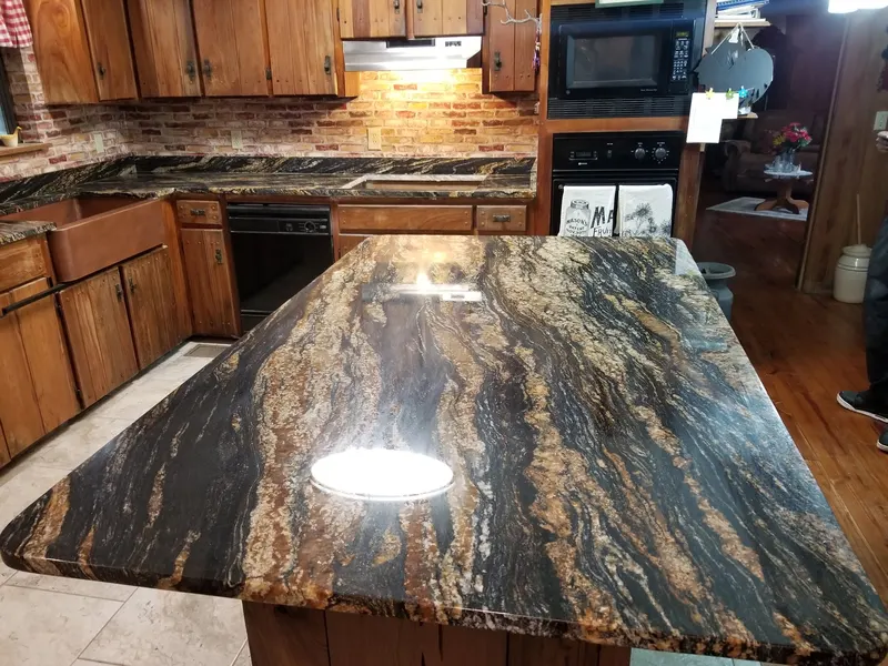 Black and gold stone island in a kitchen with wood cabinets and a brick backsplash