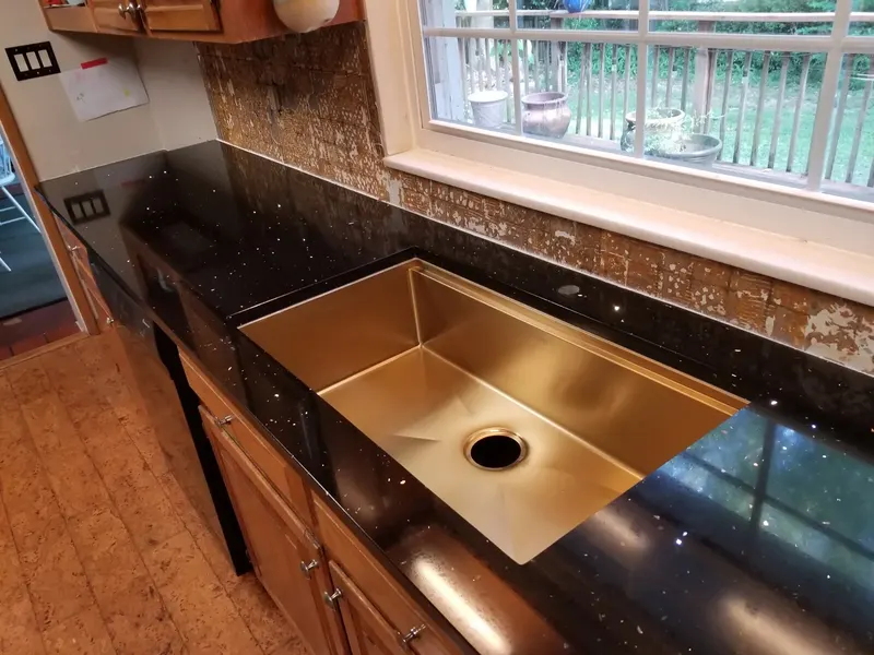 Black sparkle counter with a long gold-toned undermount sink beneath a window