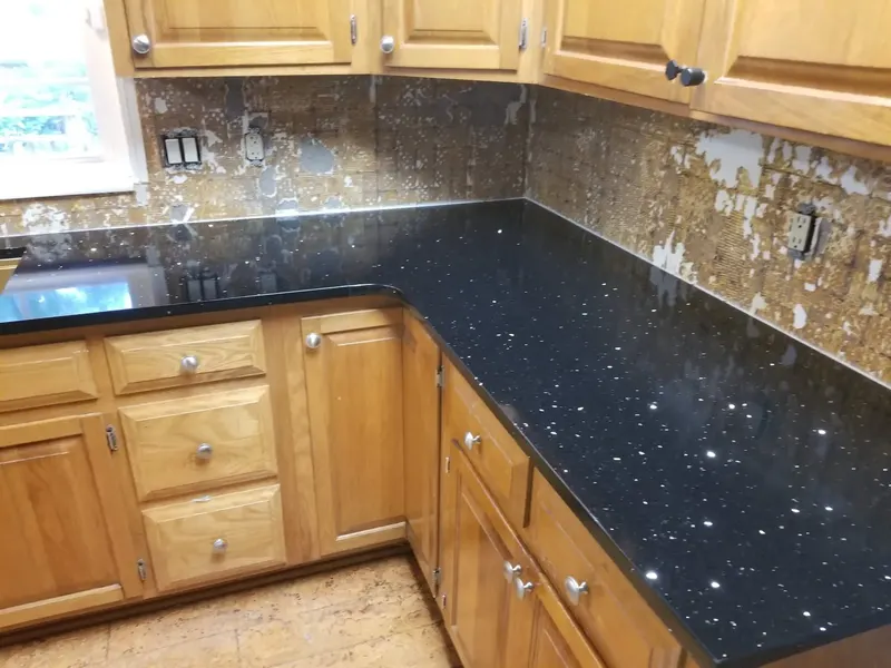 Black counter with tiny sparkles in an L shape against honey oak cabinets and a mosaic backsplash