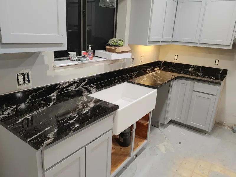 Black veined stone countertops around a white farmhouse sink with gray cabinets