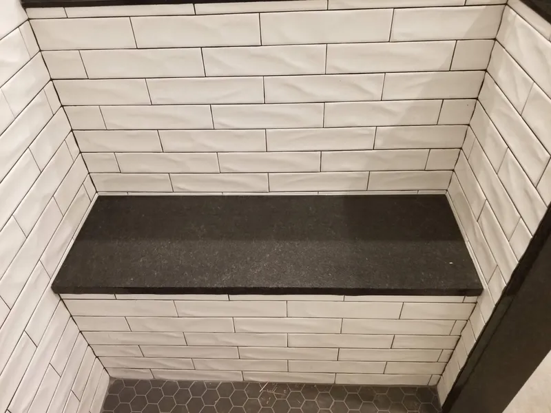 Black stone bench seat in a white subway tile shower