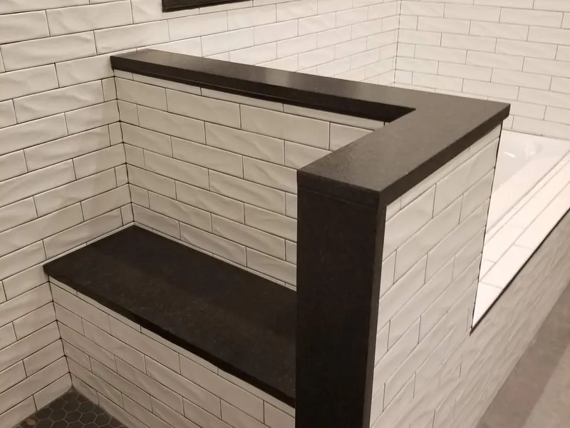 Black stone shower bench and a black stone cap on the half wall beside it