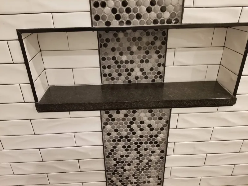 Black stone shelf and frame in a shower niche with a mosaic tile strip