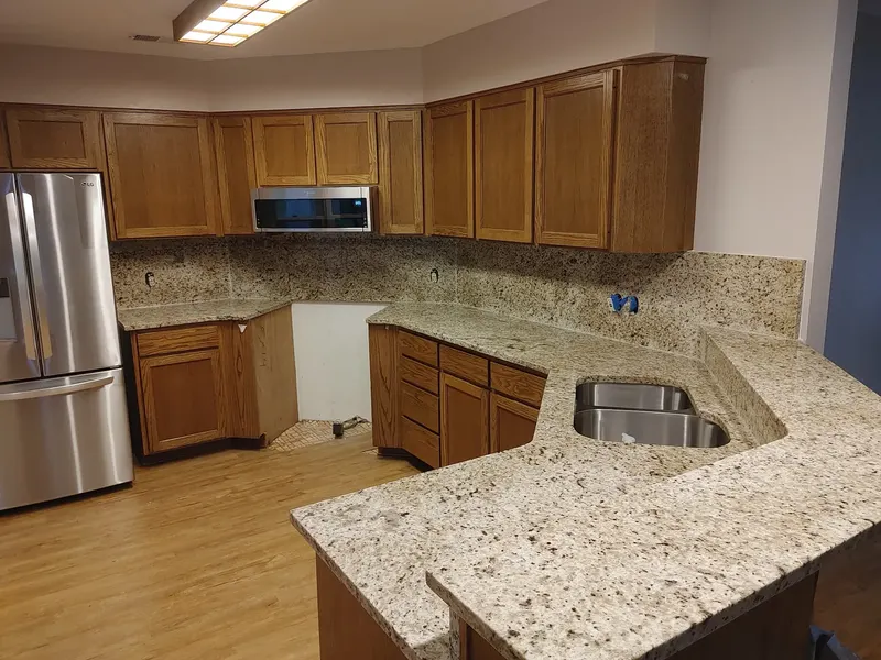 Cream counter with brown speckles, a stainless undermount sink and a matching backsplash with oak cabinets