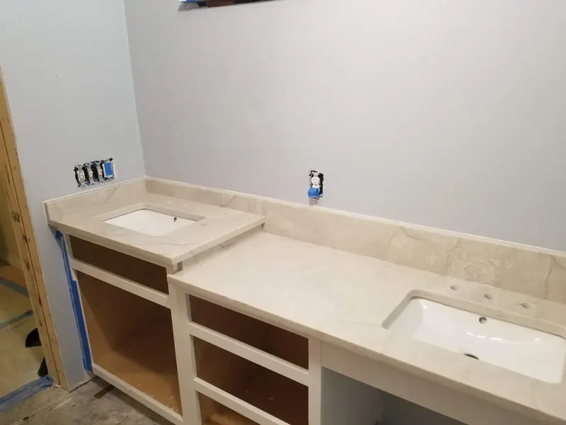 Cream stone vanity top with two white undermount sinks and a low backsplash