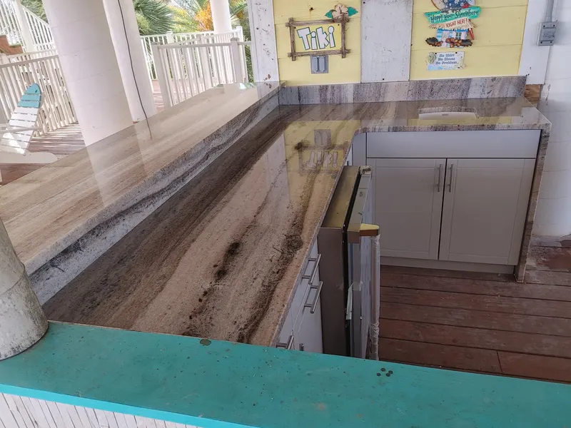 L-shaped brown and gray veined stone counter over white cabinets on a covered deck