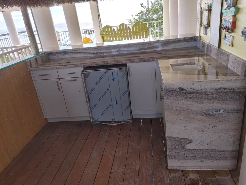 L-shaped veined stone counter with white cabinets and a stainless under-counter appliance on a covered deck