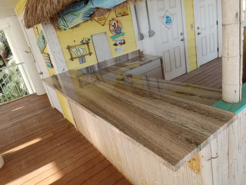 Long brown and gray veined stone counter on a wood deck bar under a thatched roof