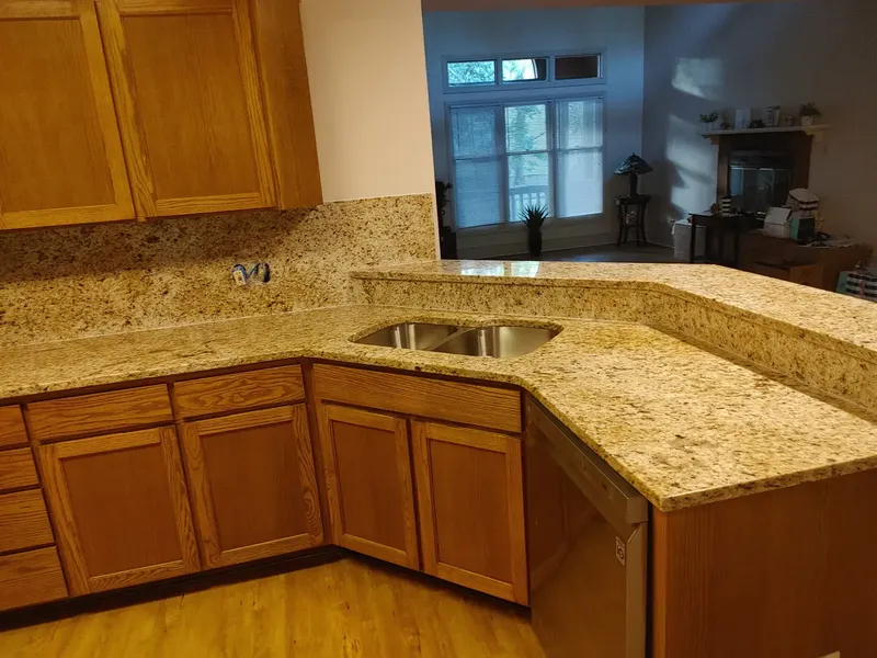 Gold and cream speckled counter with a raised bar ledge and a double sink beside oak cabinets