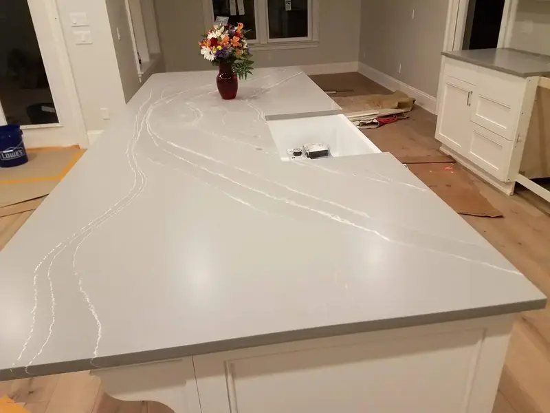 Long light gray island with thin white veins and a sink over white cabinets