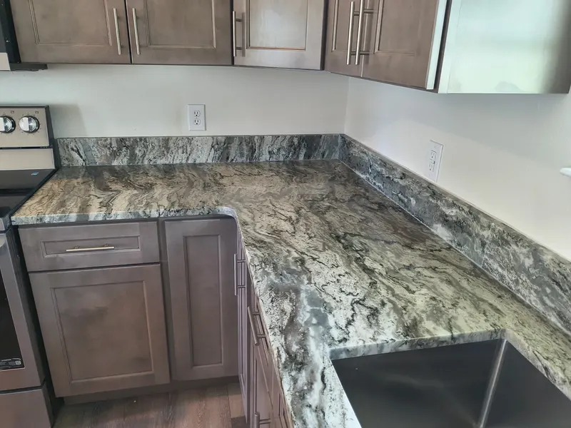 L-shaped kitchen counter in gray stone with dark veins and a matching backsplash against brown cabinets