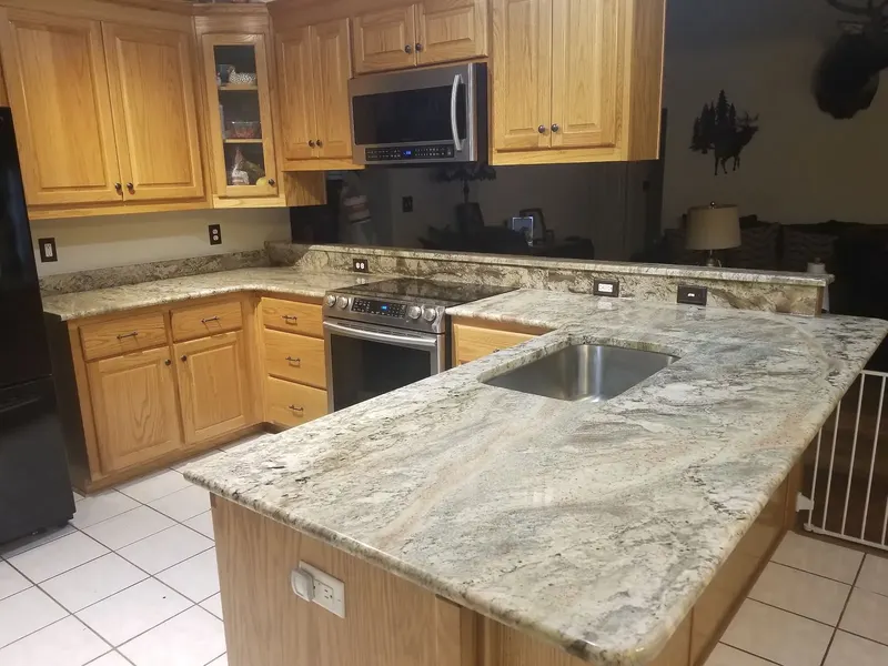 Light stone peninsula with gray and tan swirls, a steel sink and oak cabinets in a bright kitchen