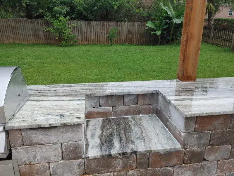 Gray and white veined stone counter and a lower side ledge on a brick paver grill station