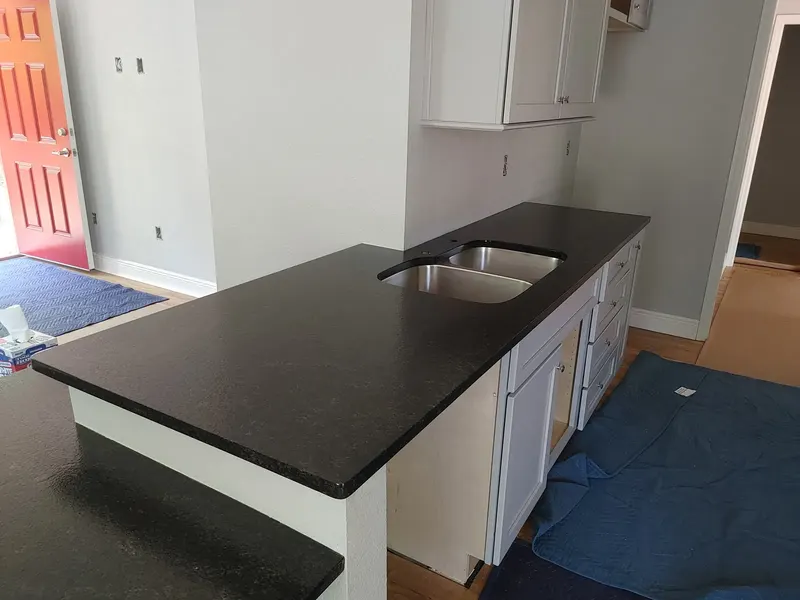 Black stone counter with a double stainless sink over white cabinets