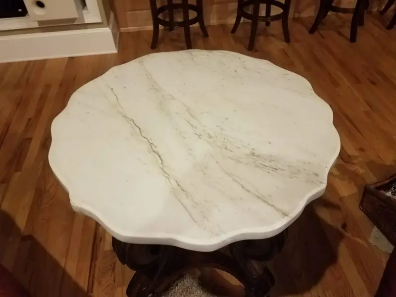 Scalloped white stone top on a round table with a carved wood base