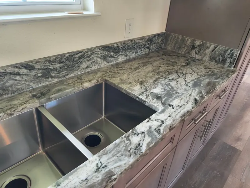 Gray and white veined counter with a large double bowl steel sink and a matching backsplash