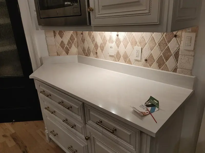 White countertop under a diamond pattern tile backsplash on gray cabinets