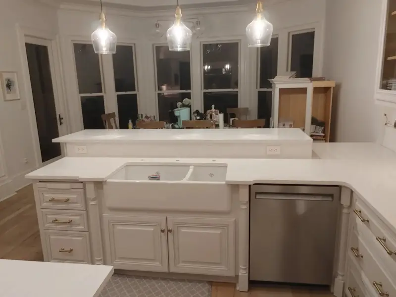 White stone kitchen countertops with a farmhouse sink under three pendant lights