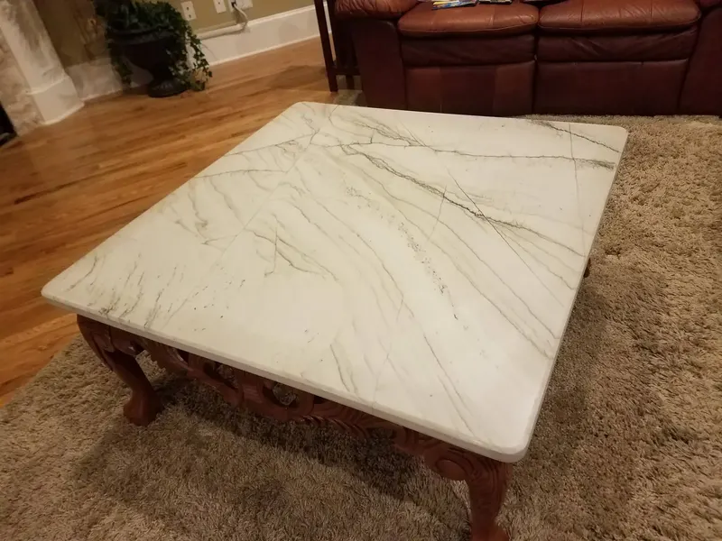 Rectangular white stone coffee table top with gray veins on a carved dark wood base