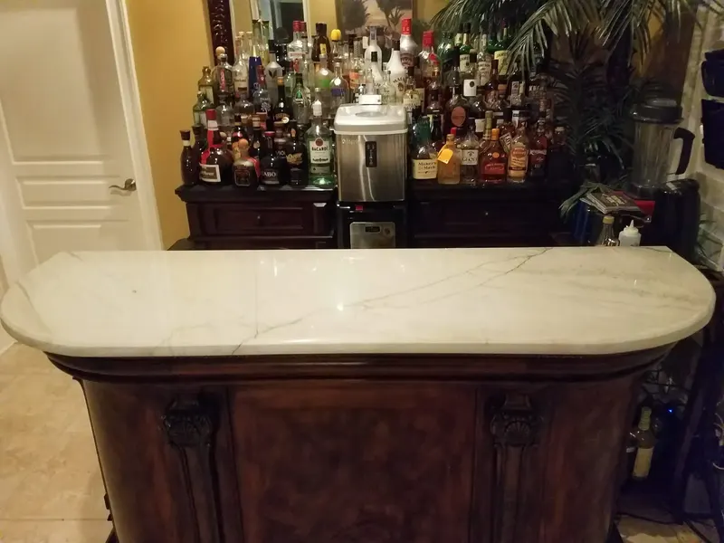 Rounded white stone bar top with thin gray veins on a dark wood cabinet